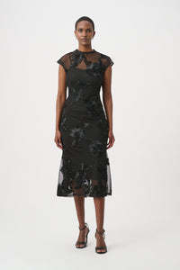 A woman modeling a black midi dress with sheer mesh cap sleeves and a floral lace overlay, paired with black strappy high-heeled sandals, against a plain light gray studio background.
