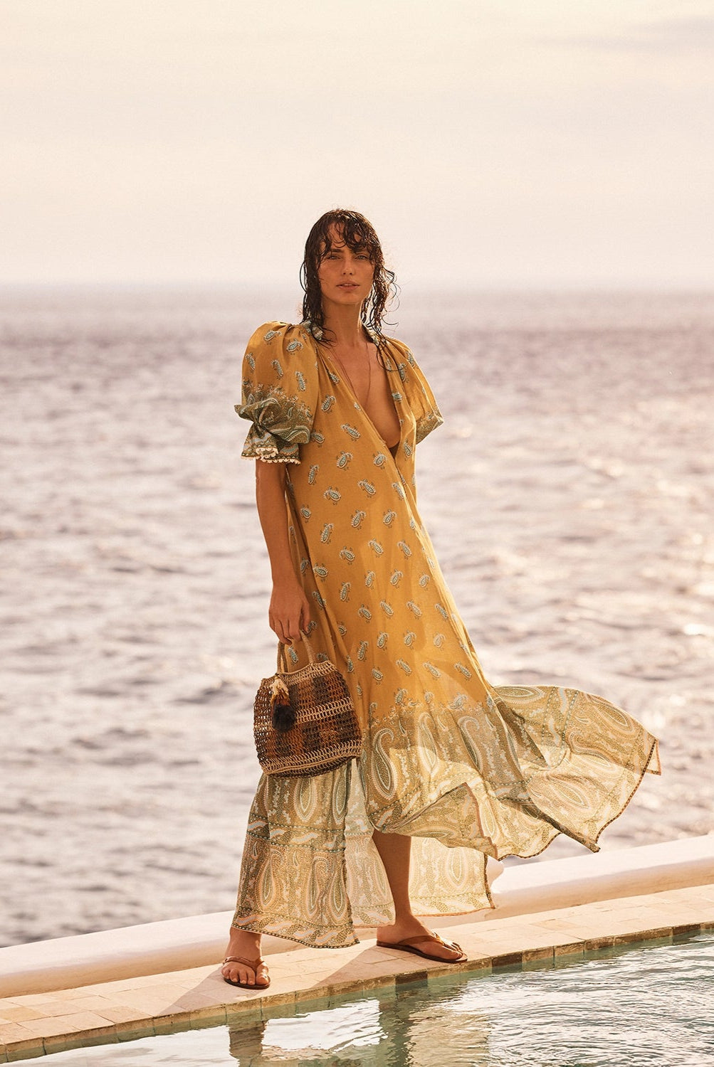 Woman in a yellow dress standing on a dock by the ocean