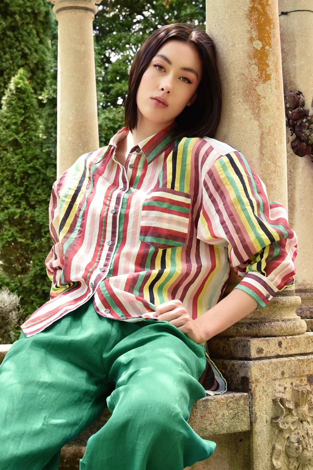 Woman wearing a colorful striped shirt and green pants sitting outdoors.